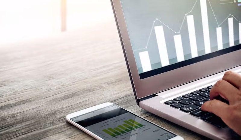 A close-up of a laptop displaying business charts and a smartphone on a desk.