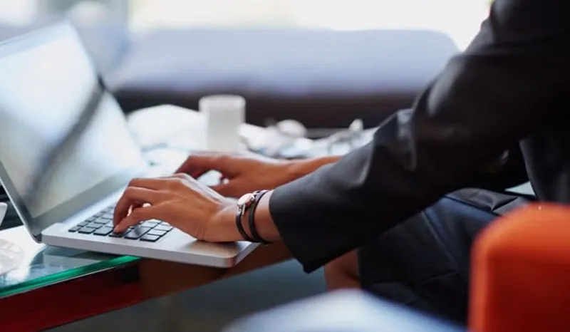 A close-up of a person typing on a laptop in a professional office setting.